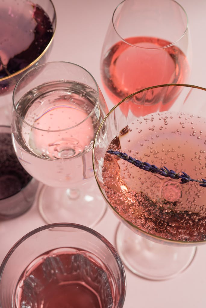 Vibrant array of sparkling wines in glasses with a light pink backdrop, perfect for celebrations.